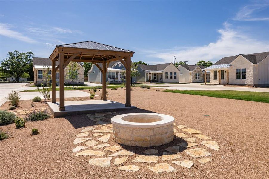 Central gazebo structure with a metal roof and concrete pad, surrounded by a stone fire pit with flagstone paving