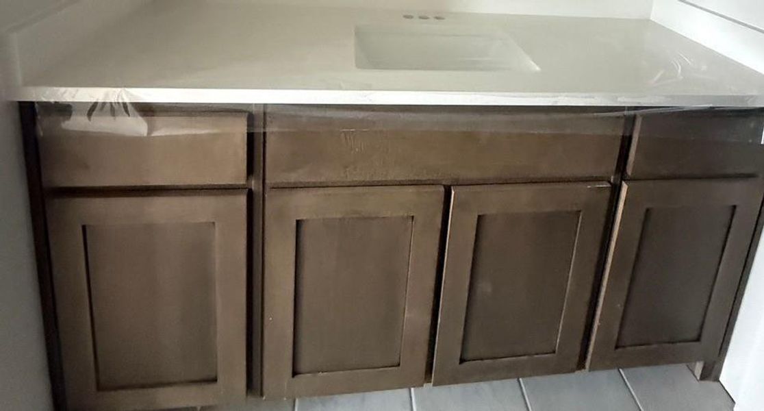 Vanity with a white integrated sink and countertop, featuring dark wood-finish cabinetry with multiple drawers and cabinet doors Vanity with a white integrated sink and countertop, featuring dark wood-finish cabinetry with multiple drawers and cabinet doors