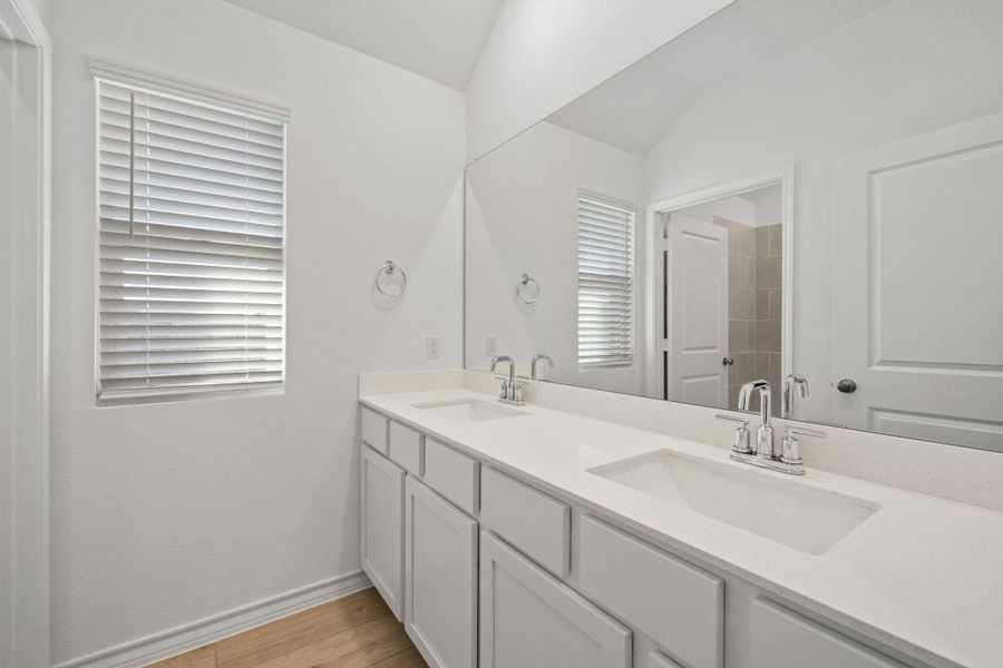 Full bath with double vanity, light wood-style floors, and lofted ceiling