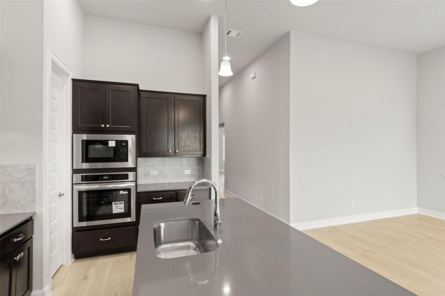 Kitchen with oven, light wood finished floors, built in microwave, backsplash, and dark brown cabinetry