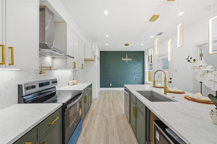 Kitchen featuring stainless steel appliances, white cabinetry, quartz countertops, wall chimney range hood, and light LVP flooring Kitchen featuring stainless steel appliances, white cabinetry, quartz countertops, wall chimney range hood, and light LVP flooring