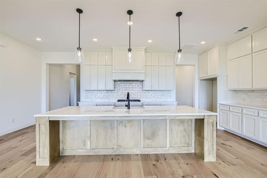 Kitchen featuring hanging light fixtures, decorative backsplash, light hardwood / wood-style floors, and a spacious island