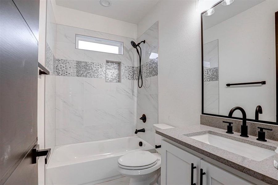 Full bathroom with vanity, tiled shower / bath combo, and toilet