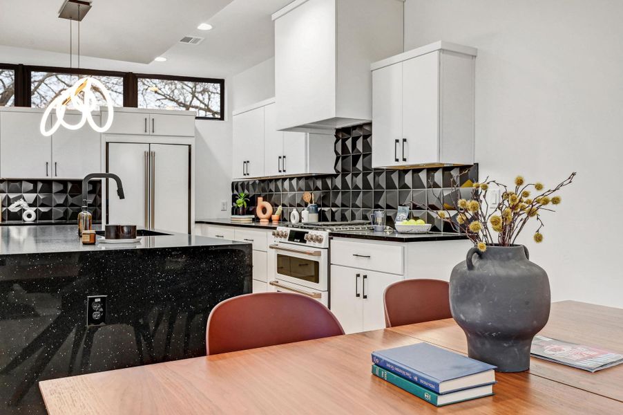 Kitchen with white cabinets, pendant lighting, decorative backsplash, high quality appliances, and dark stone counters