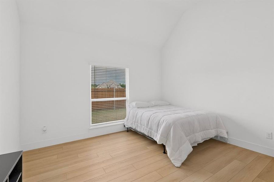 Bright room featuring a vaulted ceiling and wood-finish flooring Bright room featuring a vaulted ceiling and wood-finish flooring