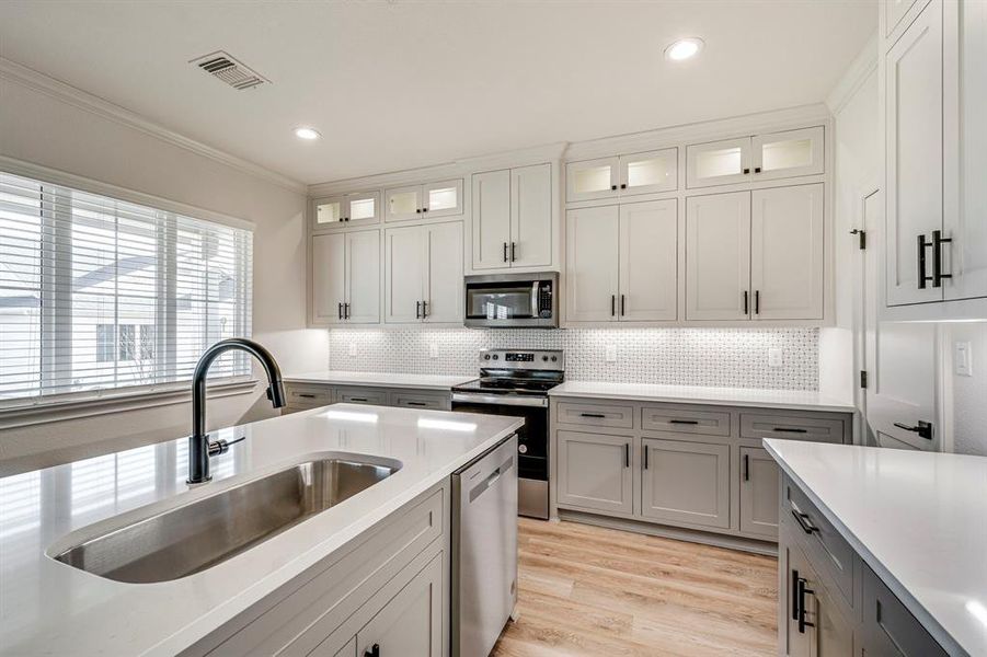 Kitchen featuring light countertops, a sink, stainless steel appliances, and gray cabinetry Kitchen featuring light countertops, a sink, stainless steel appliances, and gray cabinetry