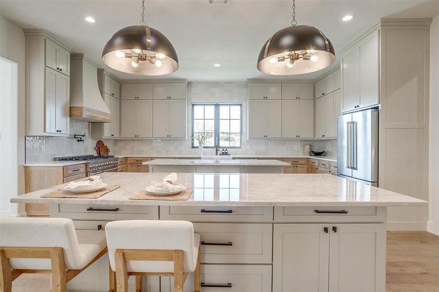 Kitchen featuring premium range hood, light stone counters, premium appliances, and light wood-type flooring