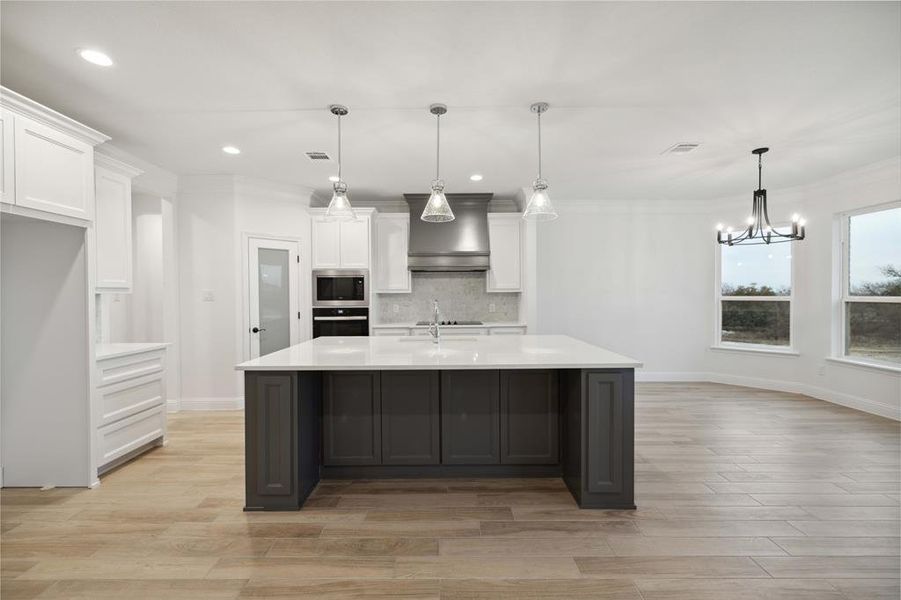 Kitchen featuring hanging light fixtures, custom exhaust hood, tasteful backsplash, white cabinetry, and appliances with stainless steel finishes