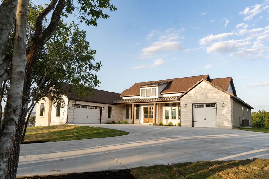 Modern farmhouse style home featuring a standing seam roof, an attached garage, a metal roof, concrete driveway, and stone siding Modern farmhouse style home featuring a standing seam roof, an attached garage, a metal roof, concrete driveway, and stone siding