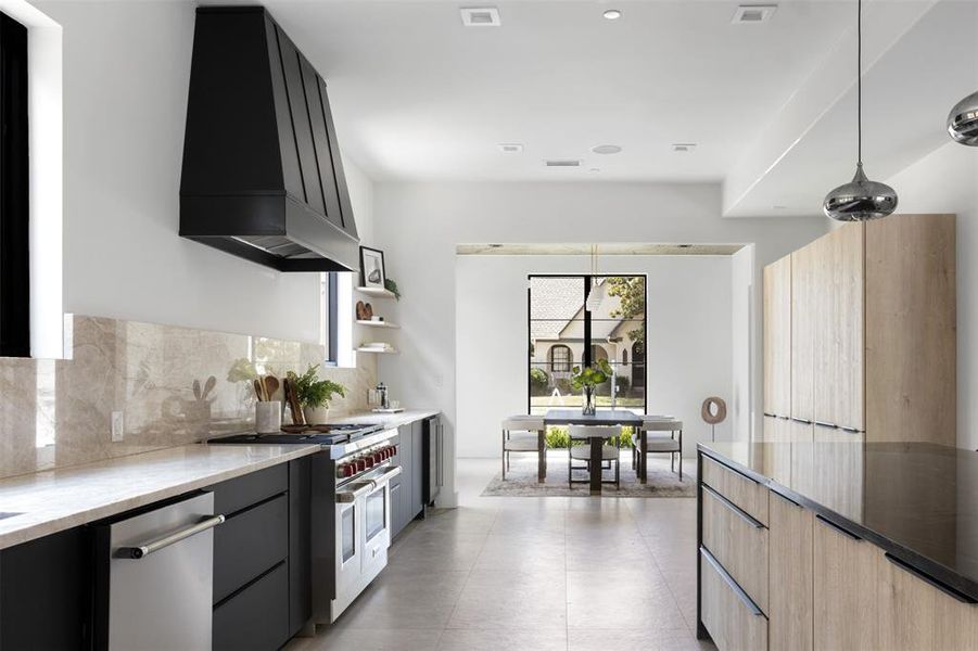 Kitchen with appliances with stainless steel finishes, light brown cabinets, premium range hood, decorative light fixtures, and light tile patterned floors