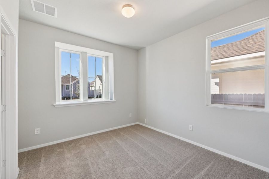 Image of a bedroom with light grey walls, tan carpeting, and windows with white trim