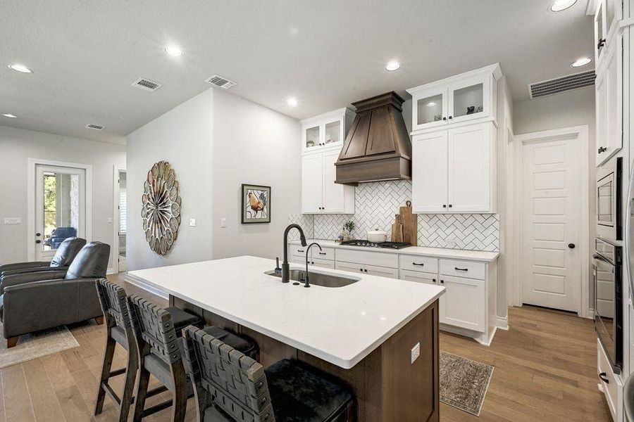 Kitchen with a kitchen bar, light wood-style flooring, white cabinetry, a center island with sink, and tasteful backsplash Kitchen with a kitchen bar, light wood-style flooring, white cabinetry, a center island with sink, and tasteful backsplash