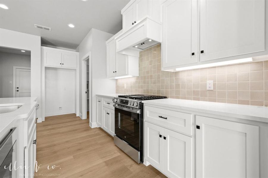 Kitchen with stainless steel appliances, white cabinets, light stone counters, light wood finished floors, and backsplash