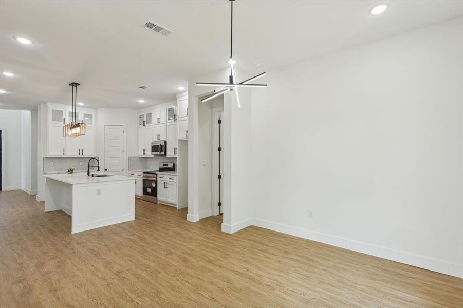 Kitchen with white cabinetry, hanging light fixtures, light wood-type flooring, and stainless steel appliances