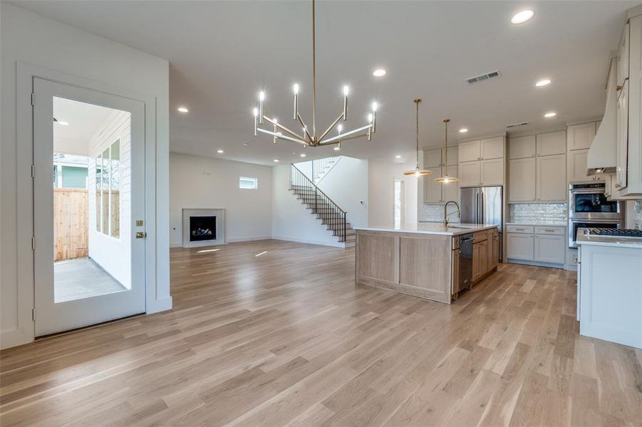 Kitchen with a large island, light hardwood / wood-style flooring, stainless steel appliances, tasteful backsplash, and decorative light fixtures