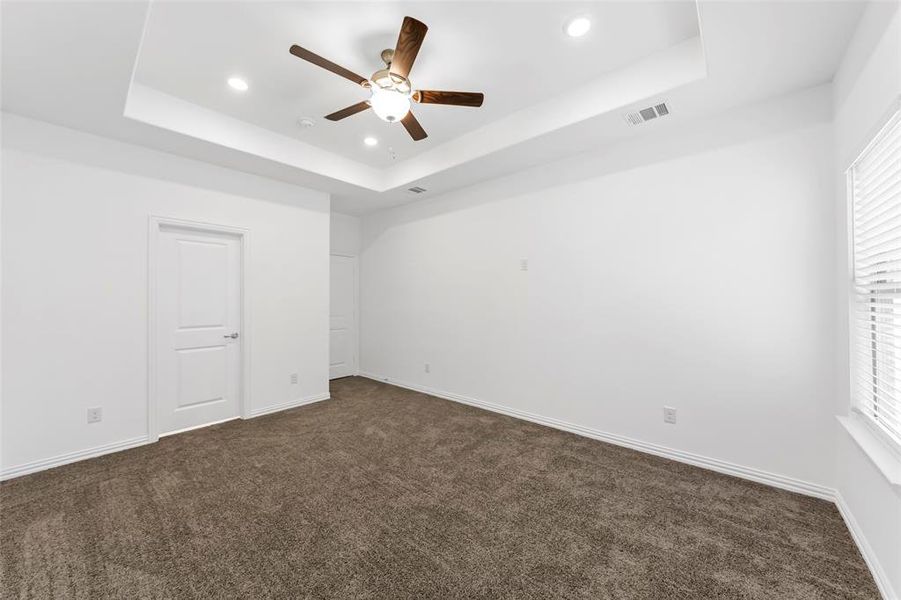 Unfurnished bedroom featuring dark carpet, a tray ceiling, and ceiling fan