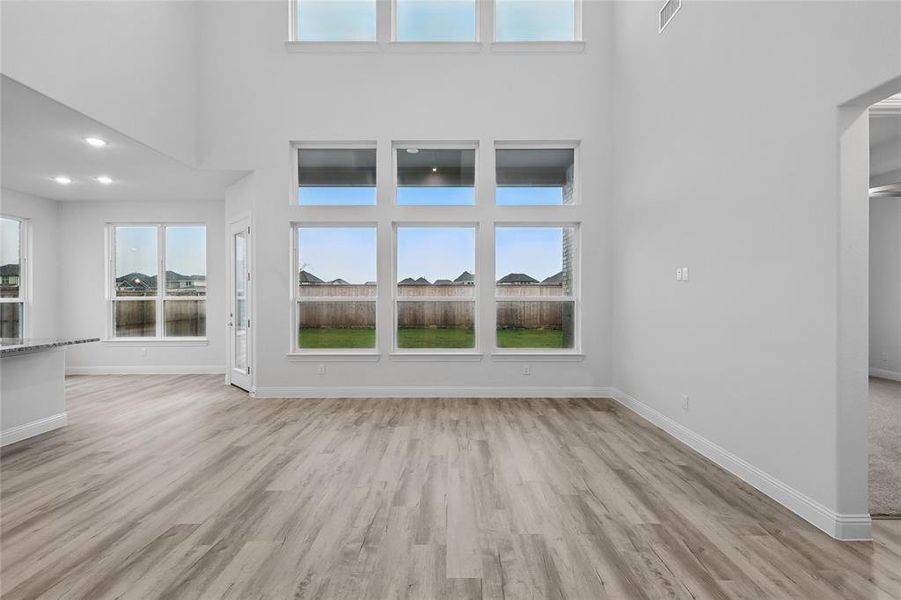 Unfurnished living room with a towering ceiling, light wood finished floors, and baseboards