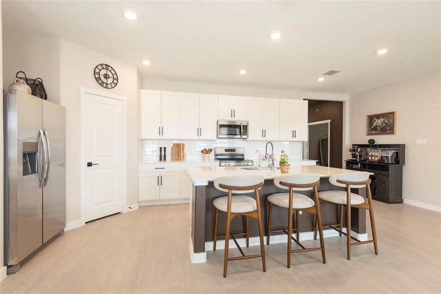 Modern kitchen featuring white shaker cabinetry, stainless steel appliances, a white subway tile backsplash, and a large island with seating Modern kitchen featuring white shaker cabinetry, stainless steel appliances, a white subway tile backsplash, and a large island with seating