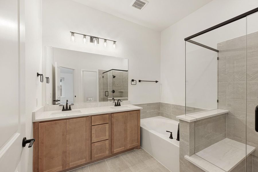 Bathroom with double vanity, wood cabinets, soaking tub, and glass walk-in shower with gray tile