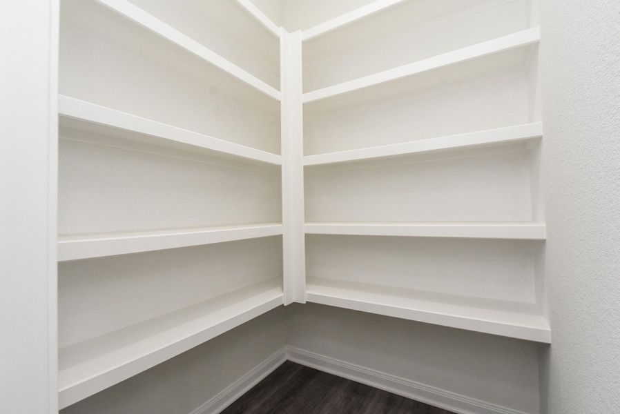 This is a clean, spacious walk-in closet with built-in white shelving and dark wood flooring, offering ample storage space in a modern design. This is a clean, spacious walk-in closet with built-in white shelving and dark wood flooring, offering ample storage space in a modern design.