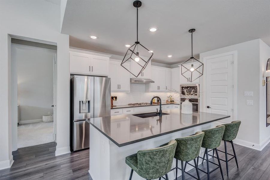 Kitchen featuring white cabinetry, stainless steel appliances, pendant lighting, a center island with sink, and a breakfast bar