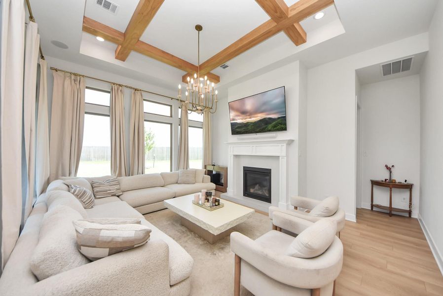 Elegant living room featuring a cozy fireplace, modern chandelier, and ample natural light, complemented by a spacious sectional sofa and stylish armchairs.