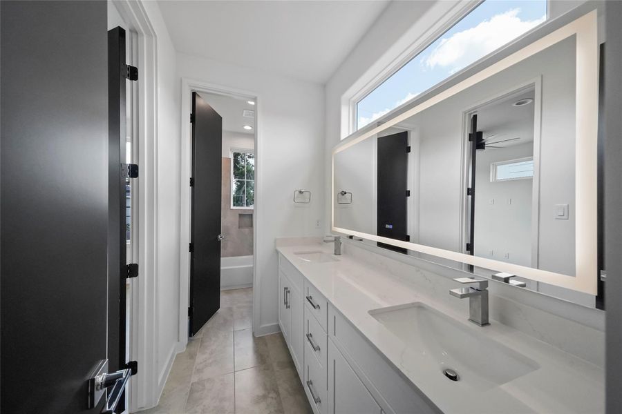 Experience modern elegance in this bathroom with a double vanity, sleek white countertops, and an illuminated mirror. The blend of natural and artificial light complements the clean lines and neutral tones, creating a serene oasis. Experience modern elegance in this bathroom with a double vanity, sleek white countertops, and an illuminated mirror. The blend of natural and artificial light complements the clean lines and neutral tones, creating a serene oasis.
