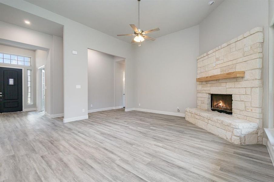 Unfurnished living room featuring a stone fireplace, ceiling fan, and light wood-type flooring