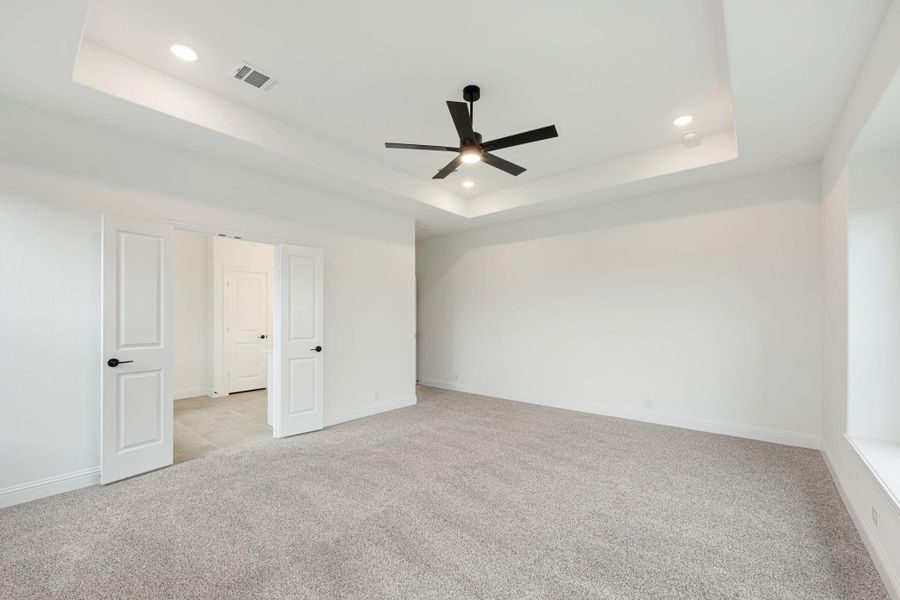Empty bedroom with tray ceiling, black ceiling fan, carpet flooring, and white walls