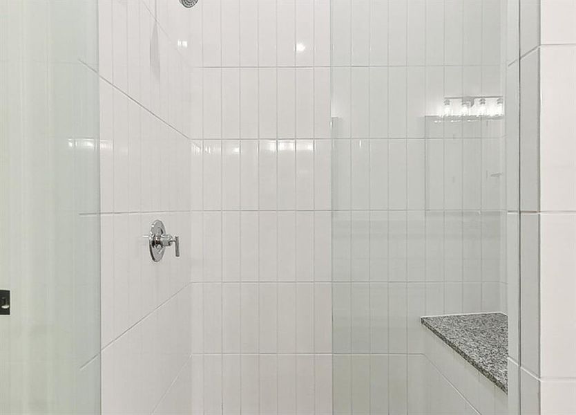 Shower with subway tile walls, chrome fixtures, and a granite corner bench