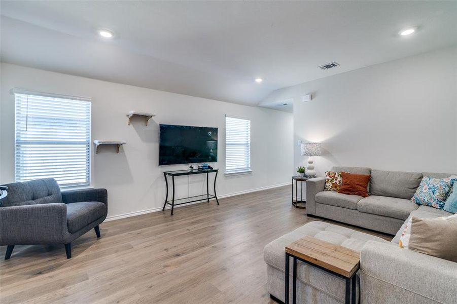 Living area featuring recessed lighting, visible vents, light wood-style flooring, vaulted ceiling, and baseboards