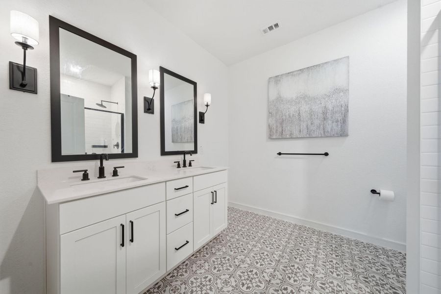 This Primary Ensuite  features a modern design with a double vanity, sleek black fixtures, and elegant patterned floor tiles. The bright space is enhanced by large mirrors, stylish wall sconces, creating a clean and contemporary look.