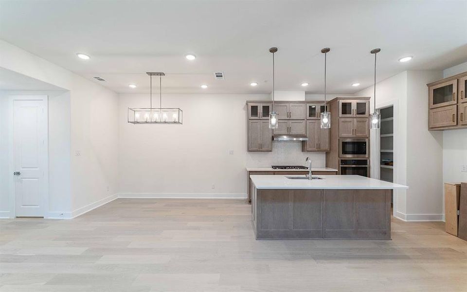 Open-concept kitchen and living area featuring light wood-finish flooring, recessed lighting, and a modern rectangular chandelier