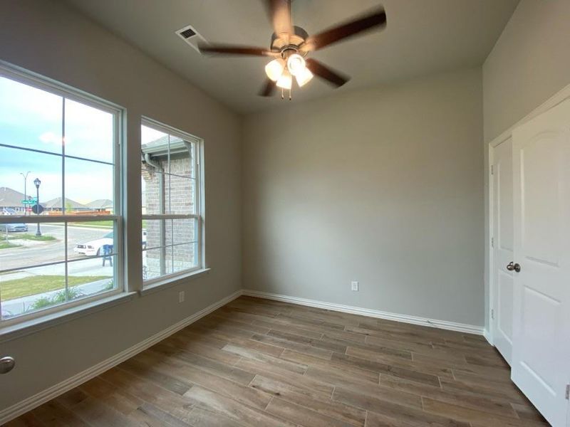 Room featuring wood-finish tile flooring, two large windows with grid patterns, a ceiling fan with integrated lighting, and neutral-toned walls Room featuring wood-finish tile flooring, two large windows with grid patterns, a ceiling fan with integrated lighting, and neutral-toned walls