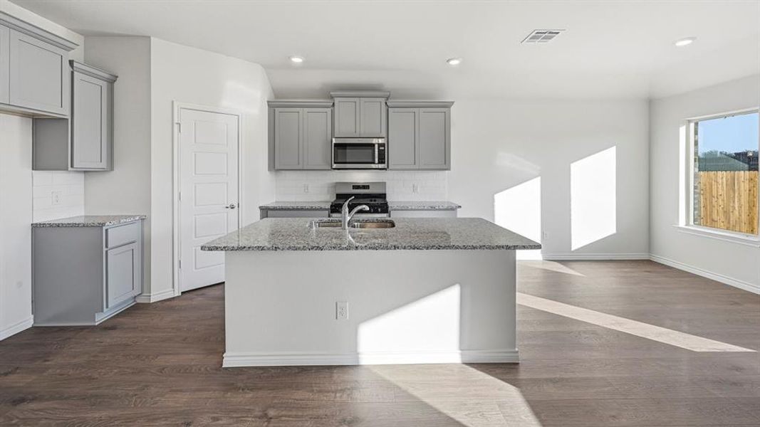 The open concept kitchen features gray cabinetry, light granite countertops, stainless steel appliances, and a central island with a sink