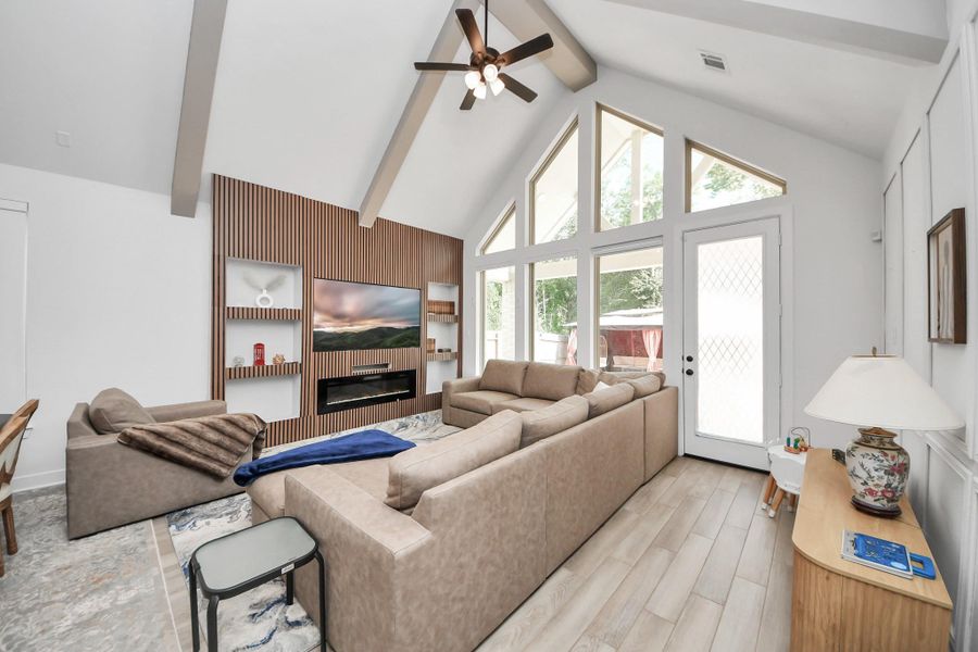 This spacious living room features high vaulted ceilings with exposed beams, a modern entertainment wall, and large windows that offer plenty of natural light. The cozy sectional sofa and sleek flooring create a warm and inviting atmosphere, perfect for relaxation and entertainment. This spacious living room features high vaulted ceilings with exposed beams, a modern entertainment wall, and large windows that offer plenty of natural light. The cozy sectional sofa and sleek flooring create a warm and inviting atmosphere, perfect for relaxation and entertainment.