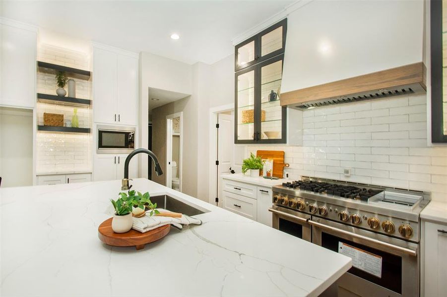 Kitchen with light stone countertops, stainless steel appliances, white cabinetry, premium range hood, and tasteful backsplash