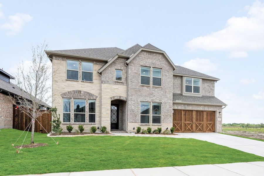 Two-story brick home with arched entry, wood garage doors, and manicured front lawn
