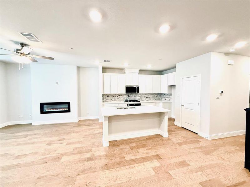 Open-concept living area featuring light wood-finish flooring, recessed lighting, and a contemporary linear electric fireplace