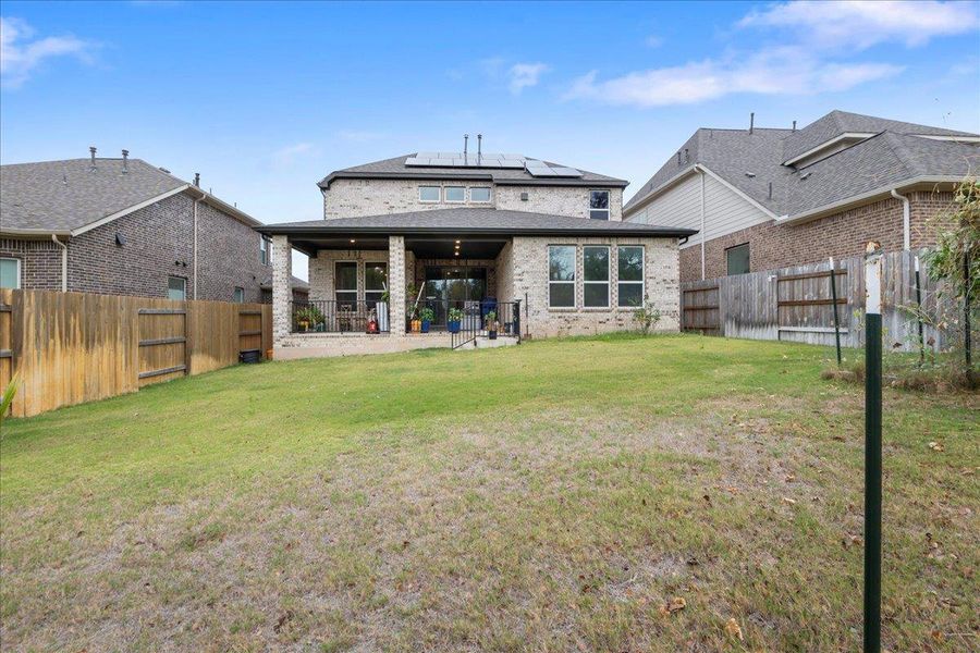 Rear view of property with brick siding, solar panels, a patio area, and a fenced backyard