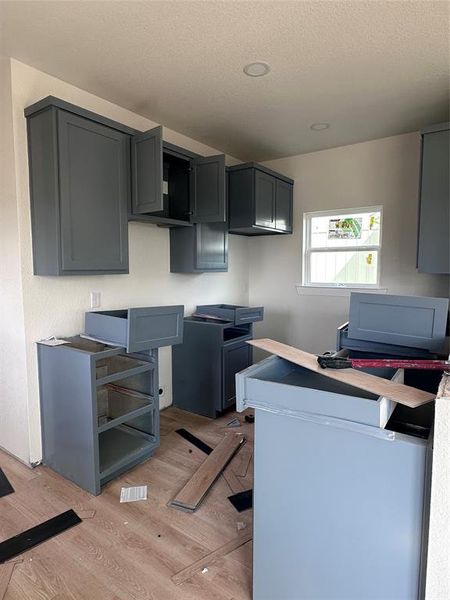 Kitchen featuring light wood-style flooring, a textured ceiling, and gray cabinets Kitchen featuring light wood-style flooring, a textured ceiling, and gray cabinets