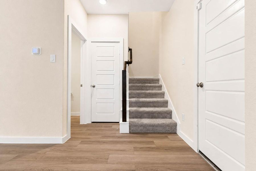 The staircase area continues the home’s clean, contemporary design with wood-look flooring, crisp white doors and trim, neutral walls, and soft carpeting on the steps. A dark-stained handrail adds contrast, while the efficient layout provides convenient access between the home’s main and upper levels. The staircase area continues the home’s clean, contemporary design with wood-look flooring, crisp white doors and trim, neutral walls, and soft carpeting on the steps. A dark-stained handrail adds contrast, while the efficient layout provides convenient access between the home’s main and upper levels.