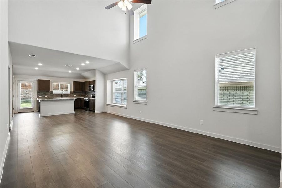 Unfurnished living room featuring a high ceiling, ceiling fan, dark wood finished floors, and recessed lighting Unfurnished living room featuring a high ceiling, ceiling fan, dark wood finished floors, and recessed lighting
