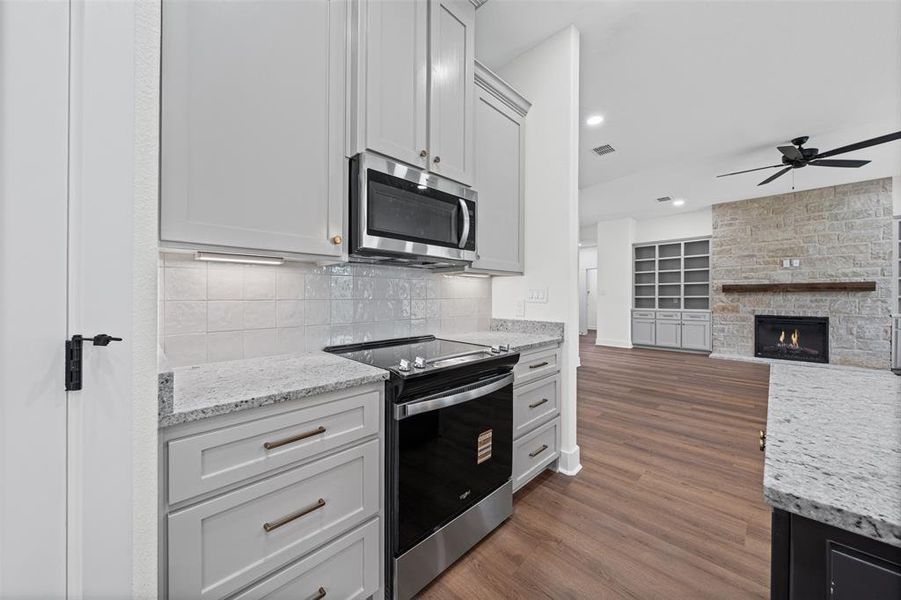 Kitchen featuring light grey cabinetry with dark hardware, granite countertops, a tiled backsplash, and stainless steel appliances