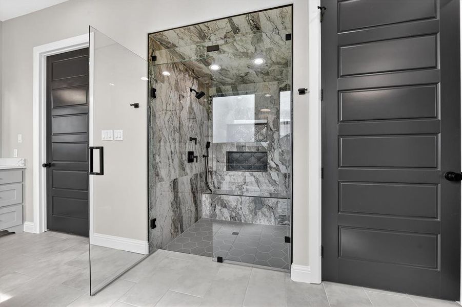 Spacious walk-in shower with floor-to-ceiling glass enclosure, large format stone-look tile, built-in bench, and multiple shower fixtures