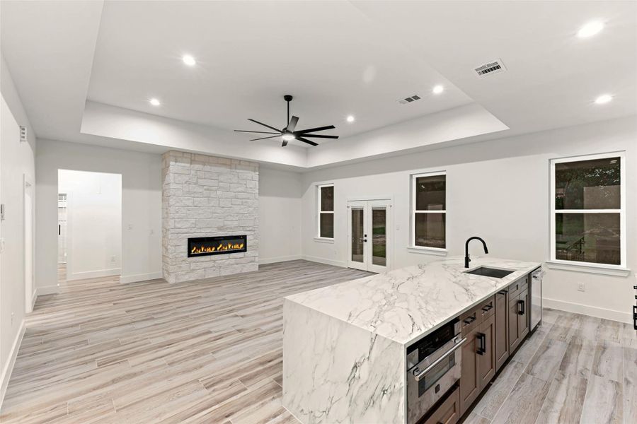 This modern living space features an open layout with a sleek kitchen island, elegant quartz countertops, and a built-in fireplace. The room is bright, with recessed lighting and large windows overlooking the backyard. This modern living space features an open layout with a sleek kitchen island, elegant quartz countertops, and a built-in fireplace. The room is bright, with recessed lighting and large windows overlooking the backyard.