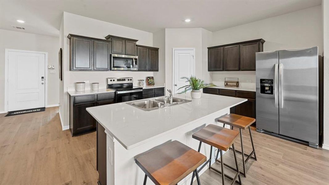 The kitchen features dark wood cabinetry, stainless steel appliances, and a central island with a white countertop and seating The kitchen features dark wood cabinetry, stainless steel appliances, and a central island with a white countertop and seating