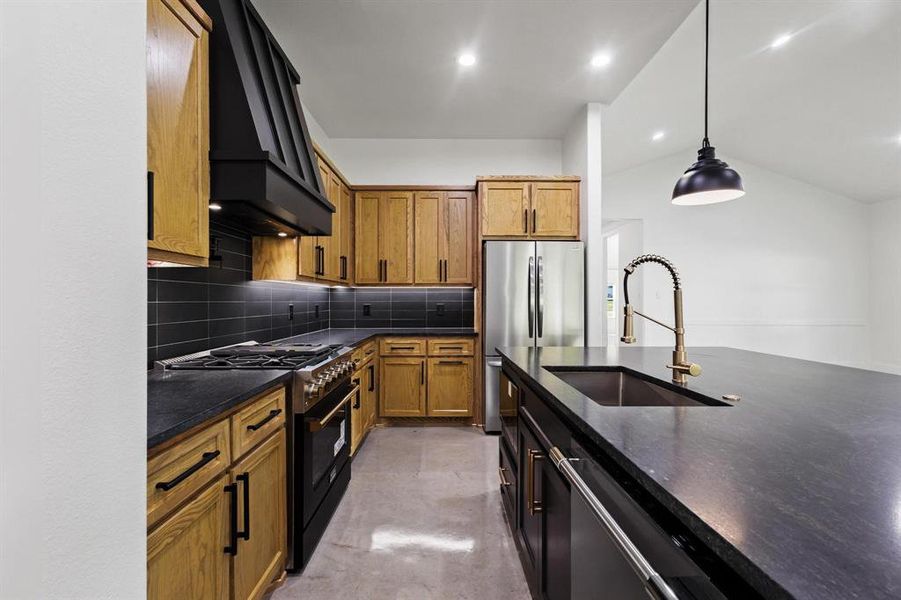 Kitchen featuring brown cabinets, tasteful backsplash, high end range, custom range hood, and hanging light fixtures