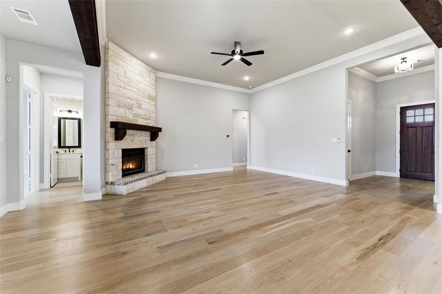 Unfurnished living room featuring light wood-type flooring, a stone fireplace, ceiling fan, crown molding, and recessed lighting