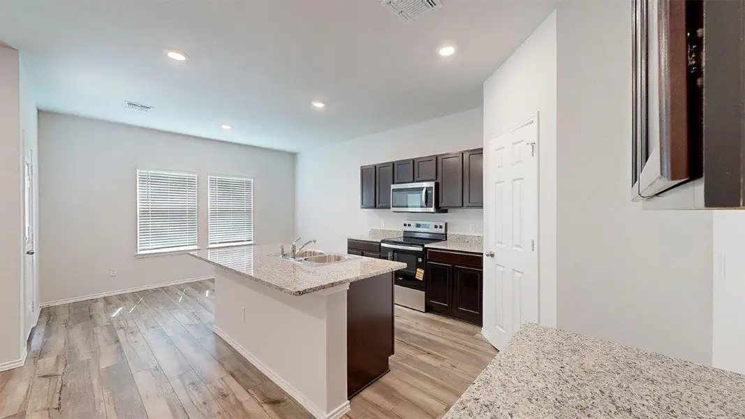 Kitchen featuring appliances with stainless steel finishes, light stone countertops, a kitchen island with sink, dark brown cabinetry, and light wood-style flooring Kitchen featuring appliances with stainless steel finishes, light stone countertops, a kitchen island with sink, dark brown cabinetry, and light wood-style flooring